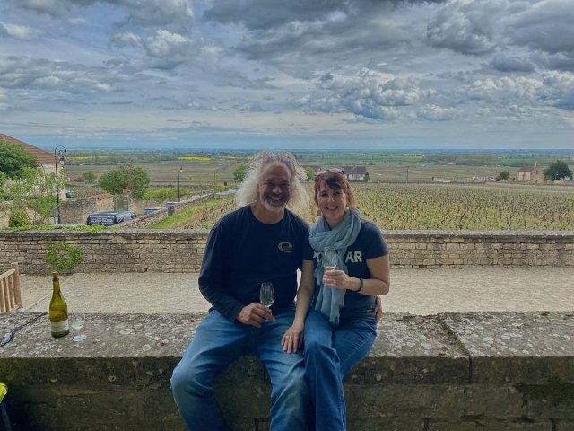 Travelers sitting on a wall with glasses of wine in front of a French vineyard in Burgundy