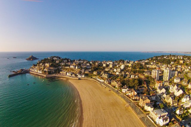 Aerial view of the beach at Le Val Andre in Brittany. The sand is golden yellow, there's a town to the right, the sea to the left is turquoise