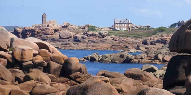 Ploumanac'h on the Pink Granite Coast The pink boulders on the Pink Granite Coast in Brittany, with a house and lighthouse in the distance, beyond the sea.