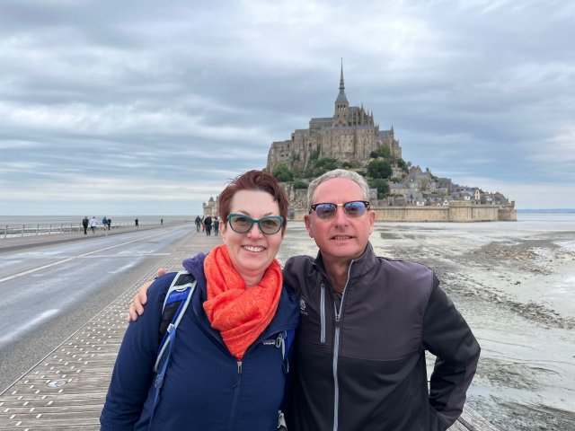 Two travelers standing on the beach in front of Mont St Michel islet and Abbey in Normandy, France