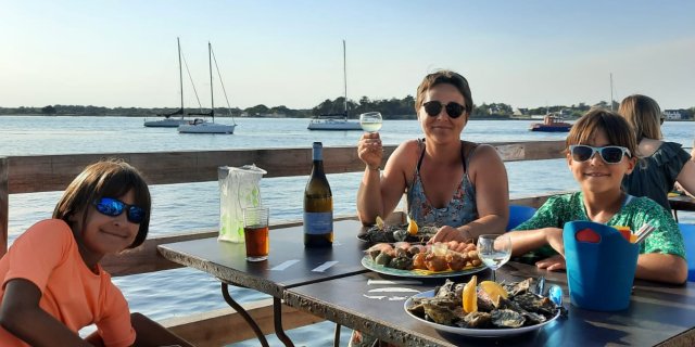 Trip planner Emilie and her 2 daughters eating oysters with lemon in Brittany, with the sea in the background