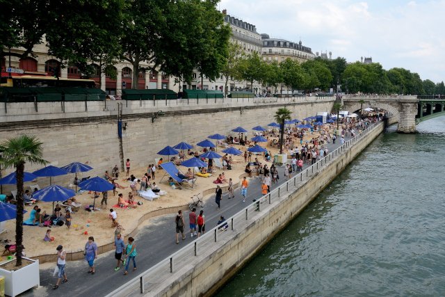 Paris Plage - a man-made beach along a stretch of the Seine river. There are people on sun loungers and blue parasols