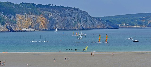 View of the sandy beach, blue sea and surrounding cliffs at the Plage de Morgat beach in Brittany