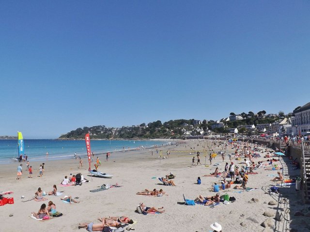 Plage de Trestraou beach in Perros-Guirec, Brittany. The sky is blue and people are sunbathing.