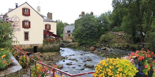 The town of Pont-Aven with a river running through it. There are yellow, red and white flowers along the river. 