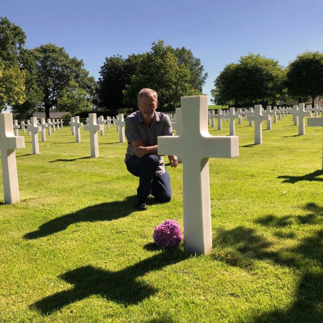 Harry from Australia kneeling in front of a grave in a war cemetery in Normandy