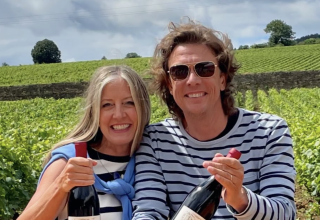 Travelers Simon & Martina in Burgundy Travelers Simon & Martina in Burgundy, holding bottles of wine with a vineyard in the background