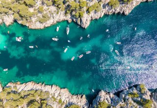 Calanque de Port Pin A birds-eye view of Calanque Port Pin. The sea is many shades of turquoise, there are boats in the sea, and the sea is surrounding by rocks and shrubs on either side