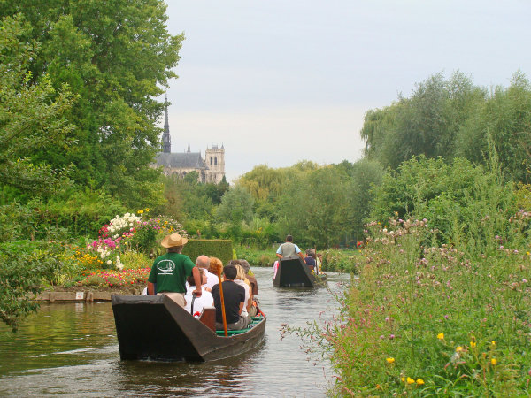 Amiens floating gardens in the Somme region of Northern France. There's a boat with people in it, and beautiful gardens on either side of the waterway.